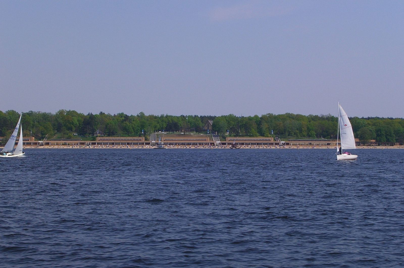 Segelboote auf dem Wannsee, im Hintergrund die langgestreckten Hallen des Strandbads Wannsee am bewaldeten Ufer
